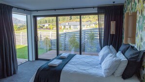 A bedroom with a large bed, a view of the outdoors, and a sliding glass door. - The Gem in Peninsula Bay (Wanaka)