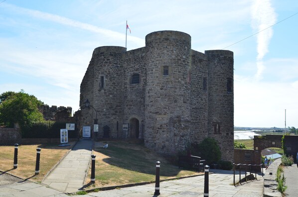 Un château historique en pierre, orné d’un drapeau, doté d’une entrée pavée et offrant une vue sur la mer.