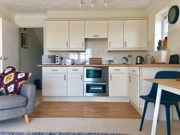 A compact kitchen with white cabinets, a microwave, a toaster, and an oven. There is a wooden countertop, a sink, and a chair. - ‘Waterside’ is a 1st floor apartment on the river in Rye, East Sussex (Rye, East Sussex)