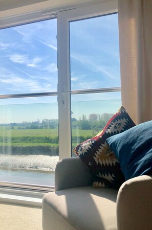 Enjoy a serene view of the surrounding landscape from the large window, featuring a comfortable seating area with a neutral-toned sofa and chair.