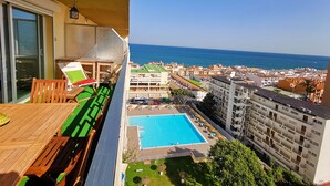 A balcony with a wooden table and chairs, a pool area with lounge chairs, and a view of the sea and buildings. - CARIHULA TORREMOLINOS APARTMENT (Torremolinos)