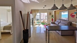 A modern living room with a sofa, a dining table, and a large window offering a view of the sea. - CARIHULA TORREMOLINOS APARTMENT (Torremolinos)
