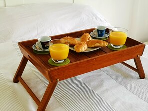 Een houten dienblad met ontbijtartikelen, waaronder croissants, sap en koffiekopjes op een bed.