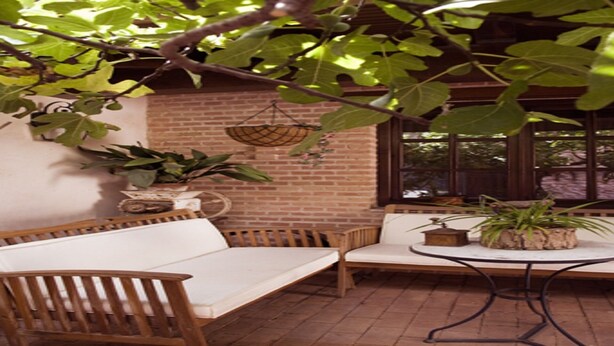 Un patio con una panchina di legno e un tavolo, circondato da piante in vaso e un muro in mattoni.