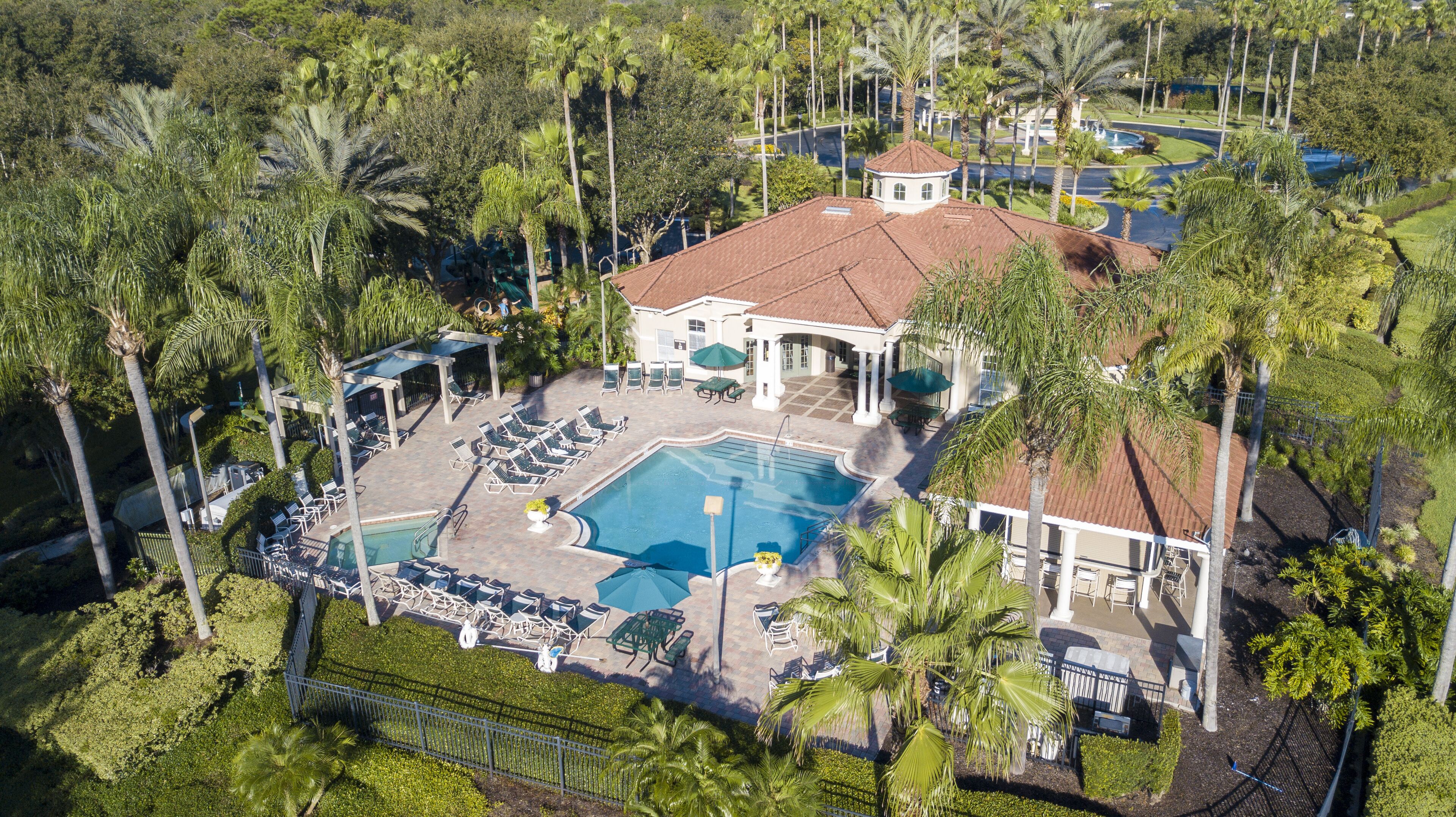 An aerial view of a resort with a swimming pool, lounge chairs, and palm trees.