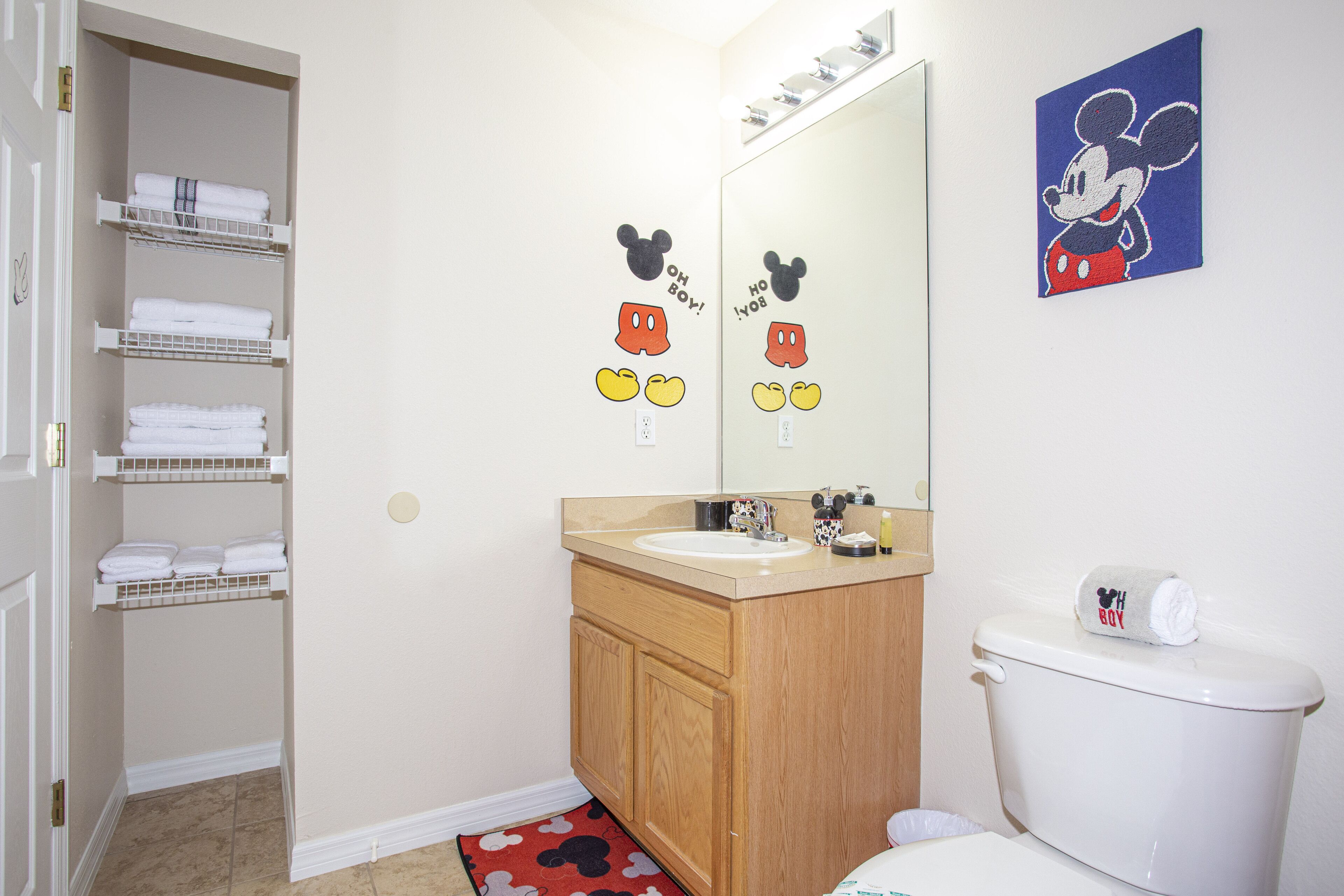 A bathroom with a wooden vanity, a white toilet, and a Mickey Mouse-themed towel holder.