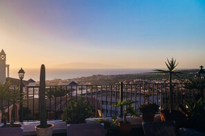 Un balcone con vista su una città costiera, tra cui edifici e una catena montuosa in lontananza.
