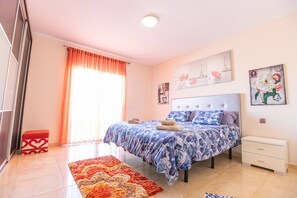 A bedroom with a bed, a nightstand, a red bench, a patterned rug, and artwork on the walls. - Villa with private pool and magnificent views of Nekhamkin (Costa Adeje)
