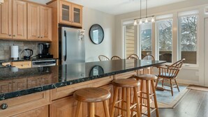 A kitchen with wooden cabinets, a stainless steel refrigerator, a large island with stools, and a view through large windows. - Walk to Gondola! - Lionshead - Outdoor Pool & Hot Tubs, Balcony + Private W/D (Vail)