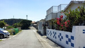 A residential street with houses, a parked car, and a clear sky. - Housei (Zamami)