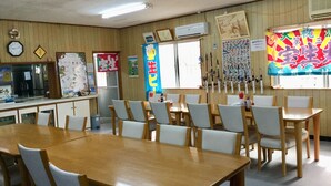A classroom with wooden tables and chairs, a clock, an air conditioner, and educational posters on the walls. - Housei (Zamami)