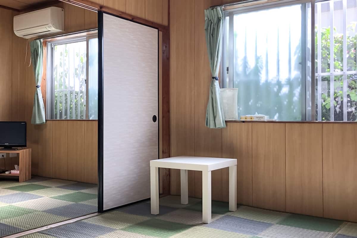 Una habitación con paredes de madera, un televisor sobre un soporte, una mesita pequeña blanca y un suelo a cuadros.