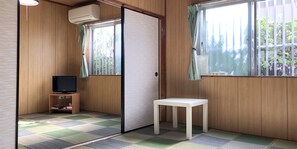 Una habitación con paredes de madera, un televisor sobre un soporte, una mesita pequeña blanca y un suelo a cuadros.