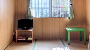 A room with wooden walls, a tatami mat floor, a television on a wooden stand, and a green bench. - Housei (Zamami)