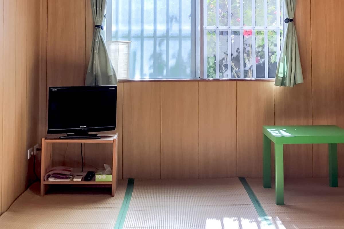 Una habitación con paredes de madera, suelo de esteras de tatami, un televisor sobre un soporte de madera y un banco verde.
