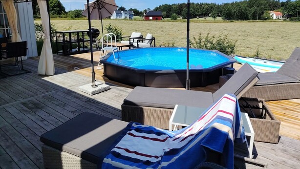 En pool med solstolar och parasoller, ett trädäck och utsikt över hus i bakgrunden.