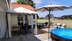 Ett trädäck med pool, utemöbler och en överbyggd sittplats.