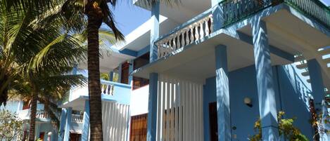 A two-story building with a balcony, surrounded by palm trees.