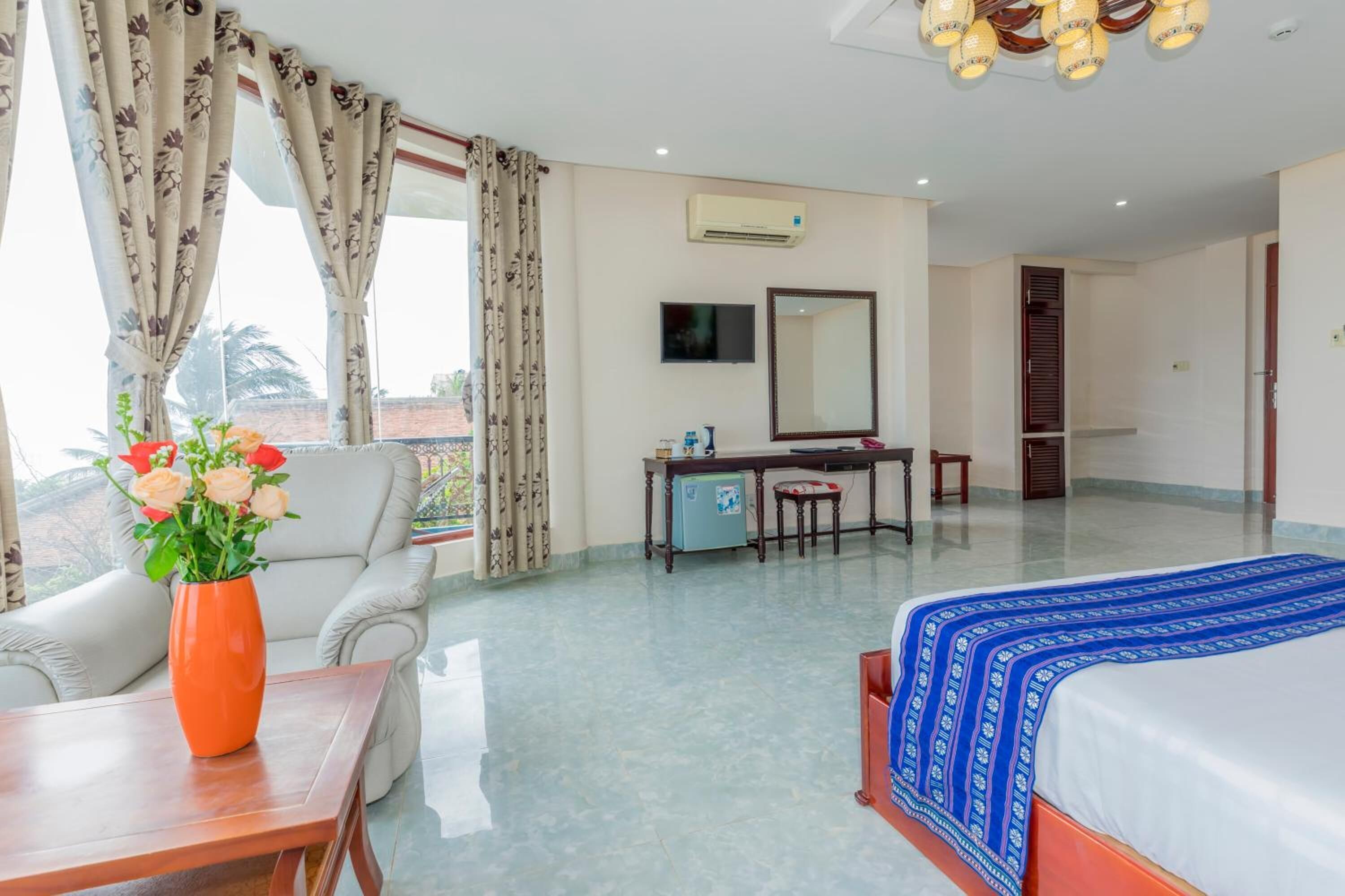 A hotel room with a bed, a desk, a chair, a TV, and a window with curtains.