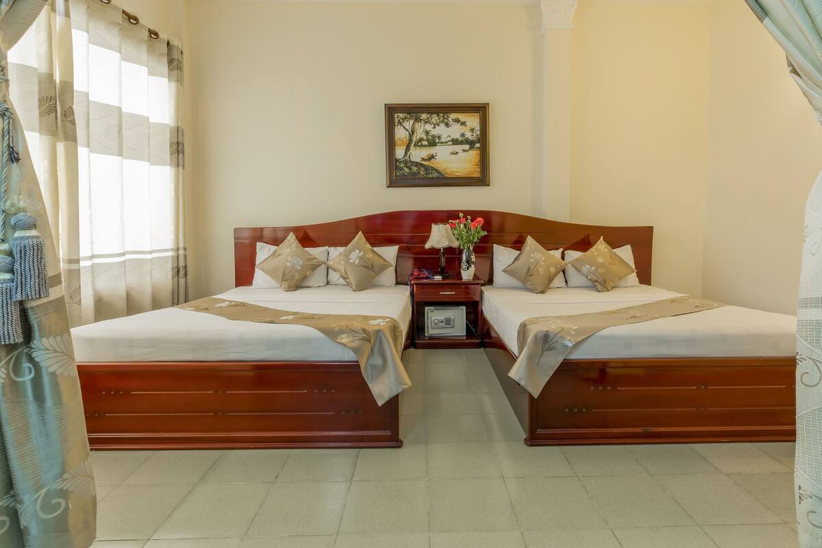 A double bed with a wooden headboard, two bedside tables, and a nightstand with a lamp and vase.