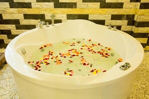 A large oval bathtub filled with water and flower petals, set against a tiled wall. - Palmira Beach Resort & Spa (Phan Thiet)
