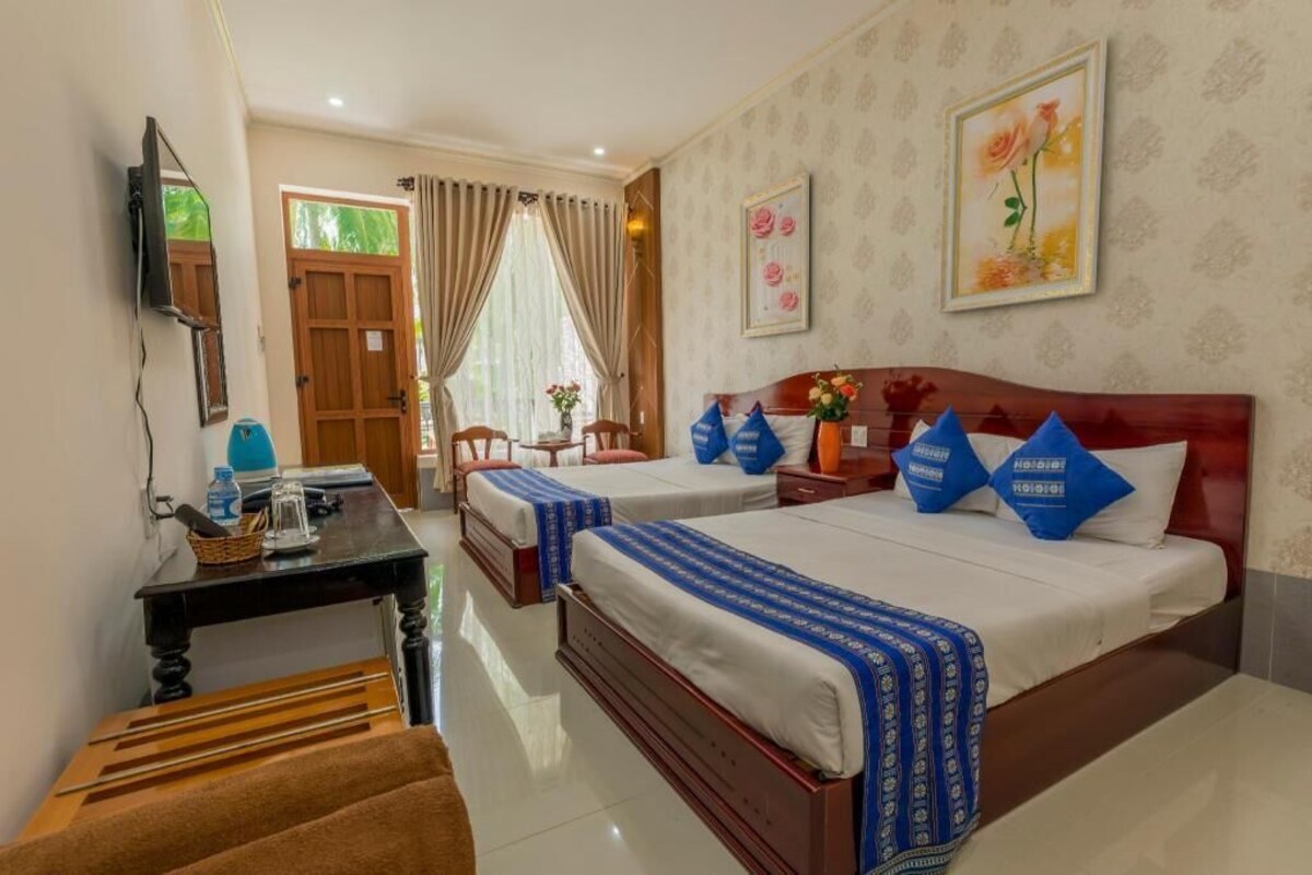 A hotel room with two beds, a desk with a lamp, a TV, and a window with curtains.