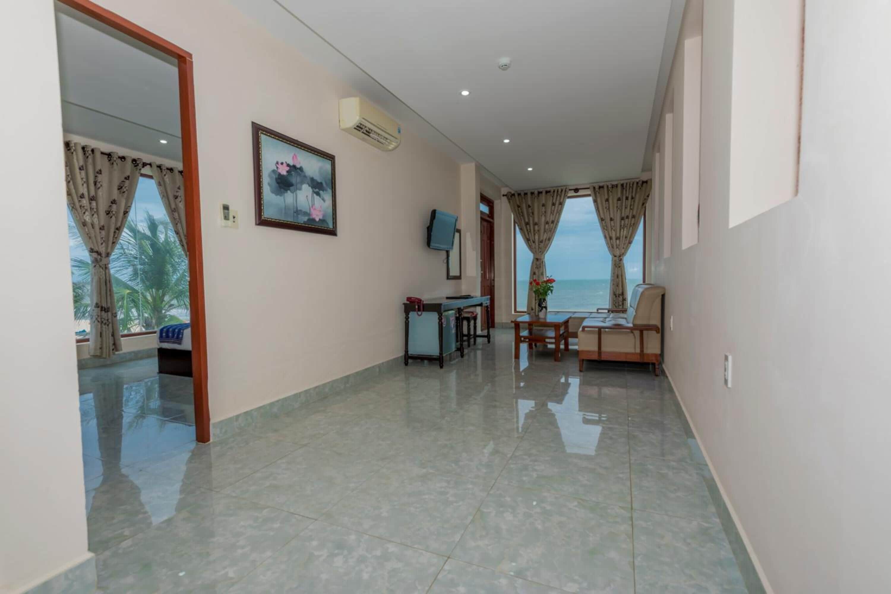 Un hall d’entrée spacieux avec vue sur la mer, un coin repas avec une table et des chaises, et un petit salon avec un téléviseur et un appareil de climatisation.