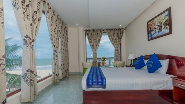 A hotel room with a bed, a desk, a chair, and a view of the beach. - Palmira Beach Resort & Spa (Mui Ne)