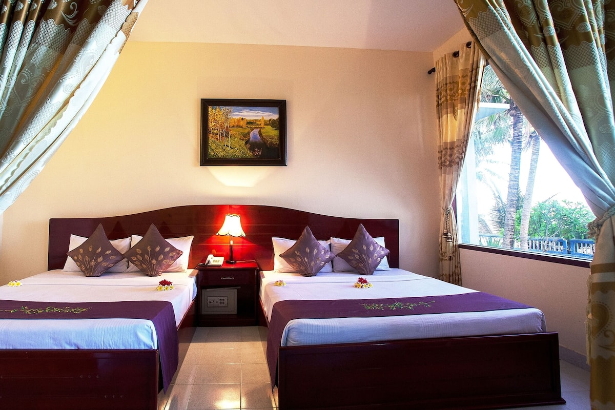 A hotel room with two beds, a nightstand with a lamp, and a framed picture on the wall.