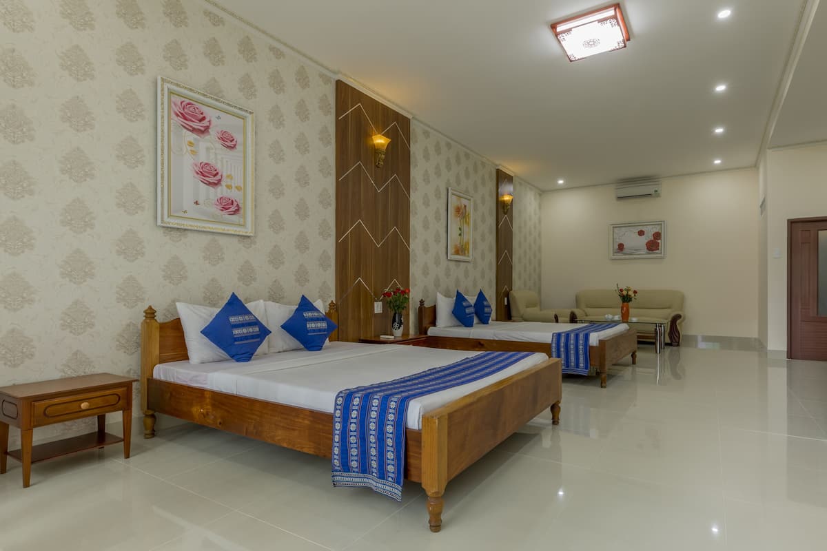 A hotel room with two wooden beds, a nightstand, a sofa, and a wall-mounted air conditioner.