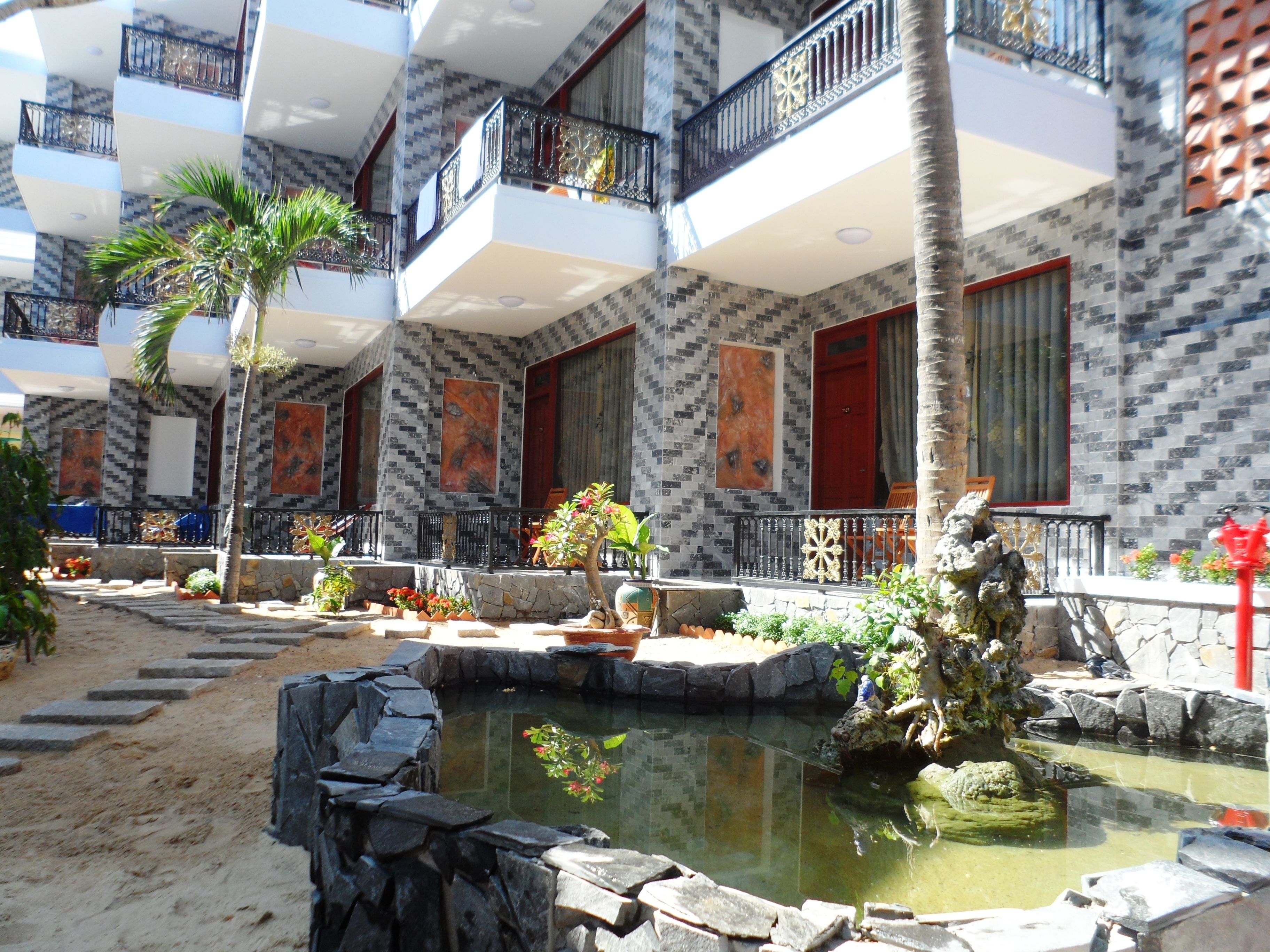 A multi-story building with balconies, a small pond, and potted plants.