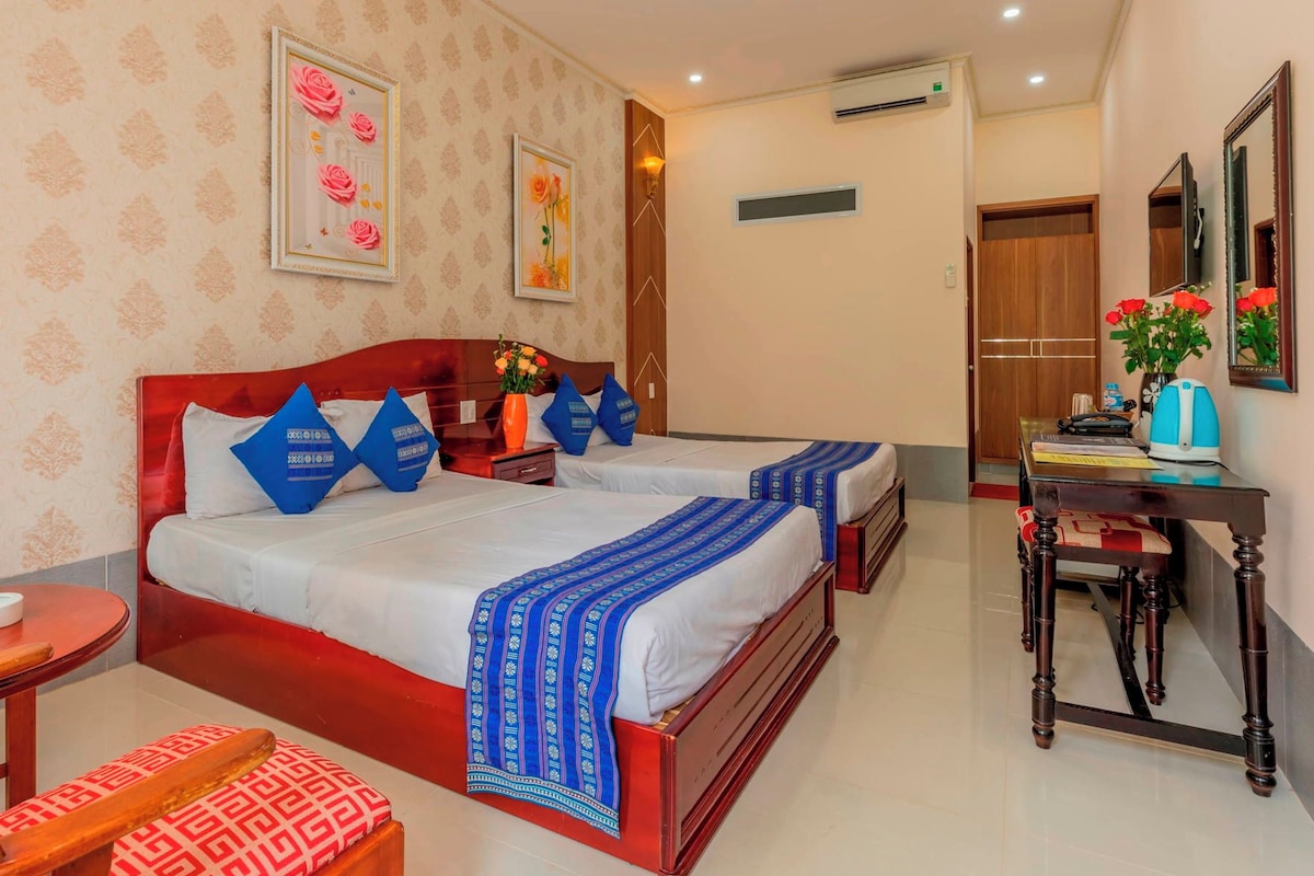A hotel room with two beds, a desk, a chair, a round table, and a TV.