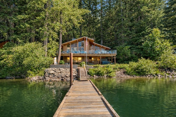A wooden cabin with a deck extending into a lake, surrounded by dense forest. - Lakefront | Dock | Hot Tub | Deck | Dogs | Views (Leavenworth)