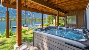Un bain à remous sous une pergola en bois, avec vue sur un lac et des montagnes.