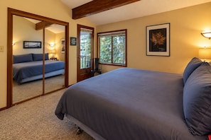 Une chambre avec un grand lit, un miroir, une porte donnant sur une autre pièce et une fenêtre avec vue sur la verdure.