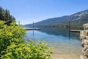 A clear lake with wooden docks extending into the water, surrounded by lush greenery and mountains in the background. - Lakefront | Dock | Hot Tub | Deck | Dogs | Views (Leavenworth)