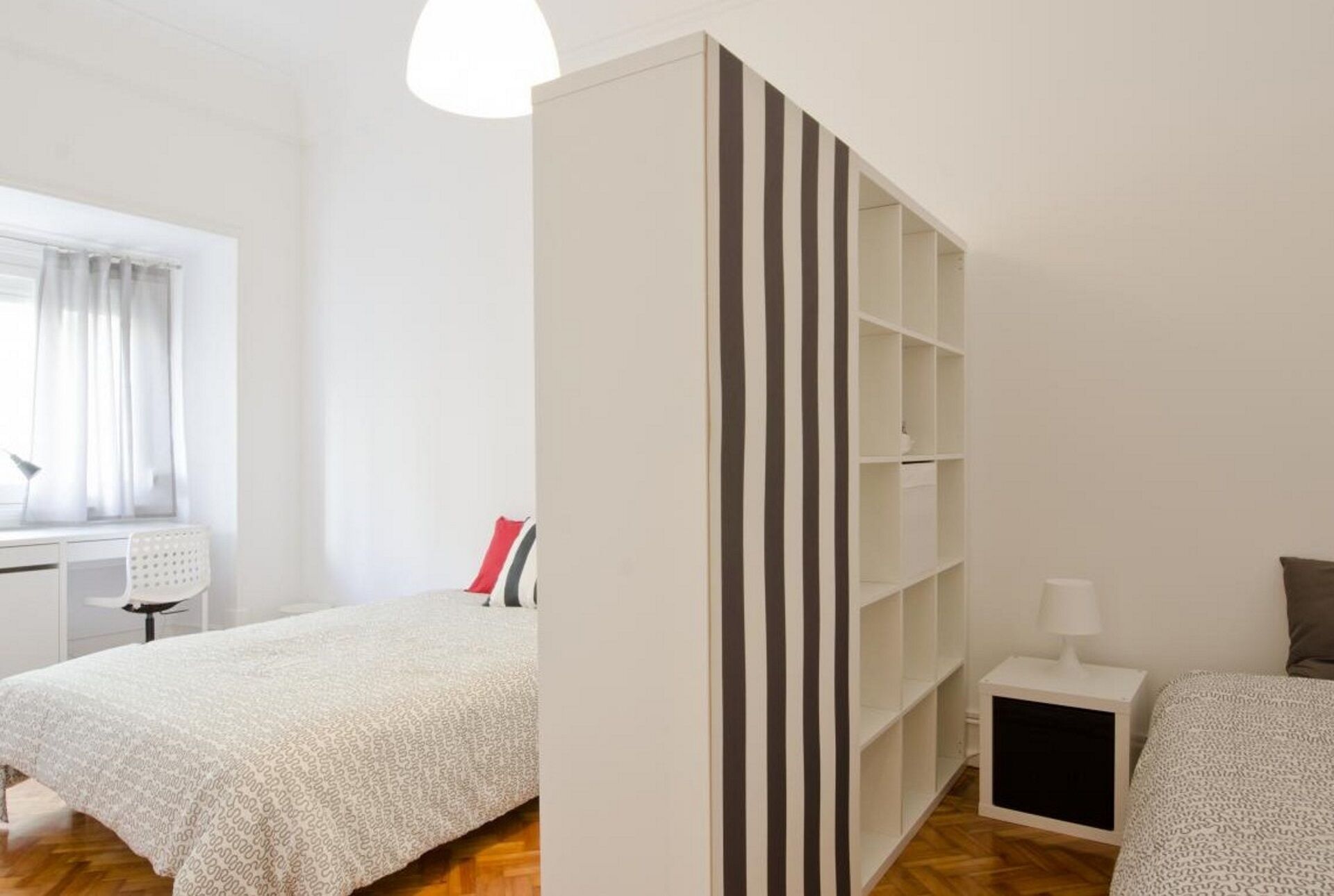 Une chambre avec deux lits, une armoire blanche, un bureau et une fenêtre avec des rideaux.