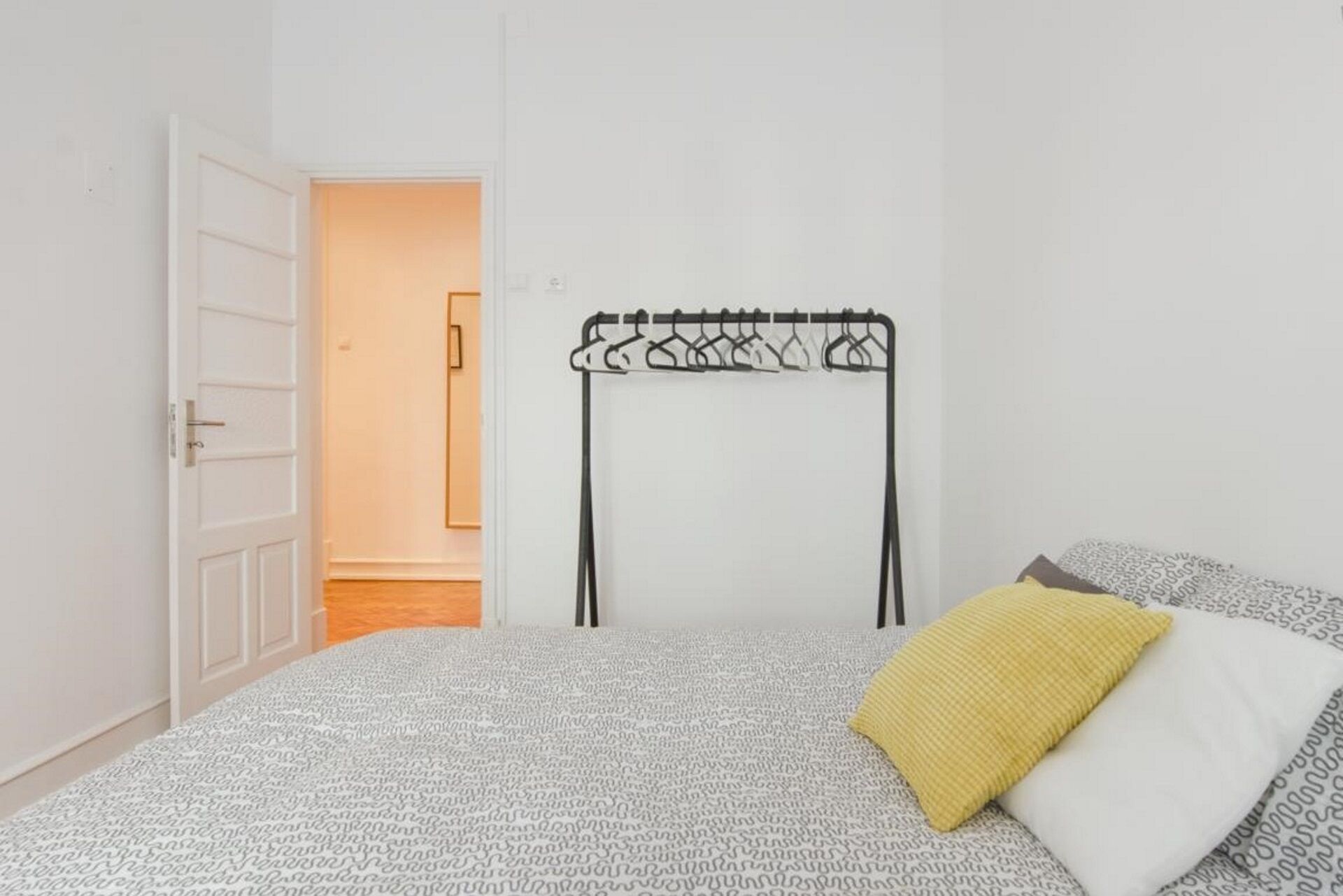 Un dormitorio con una colcha estampada, un perchero y una puerta que da a otra habitación.