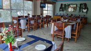 A dining area with multiple tables and chairs, some with white tablecloths and others with patterned ones. There are decorative vases with flowers on the tables. - Centennial Hotel 2008 (Phuntsholing)