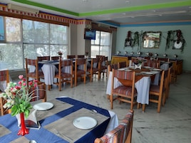 A dining area with multiple tables and chairs, some with white tablecloths and others with patterned ones. There are decorative vases with flowers on the tables.