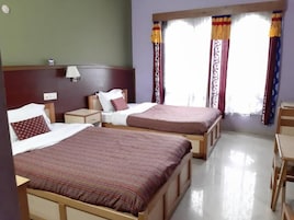 A hotel room with two beds, a nightstand, a lamp, and a window with curtains.