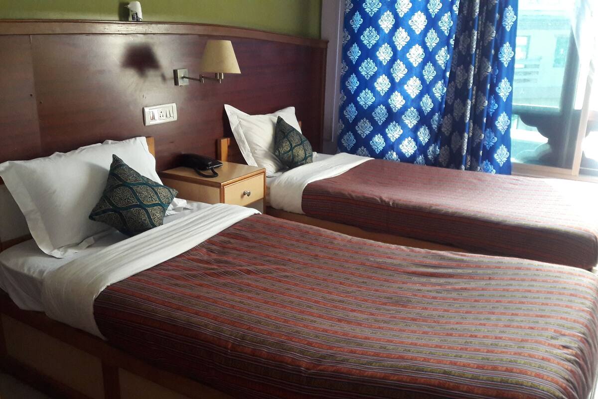 A hotel room with two beds, each with striped bedding, a wooden headboard, a bedside table with a lamp, and a telephone.