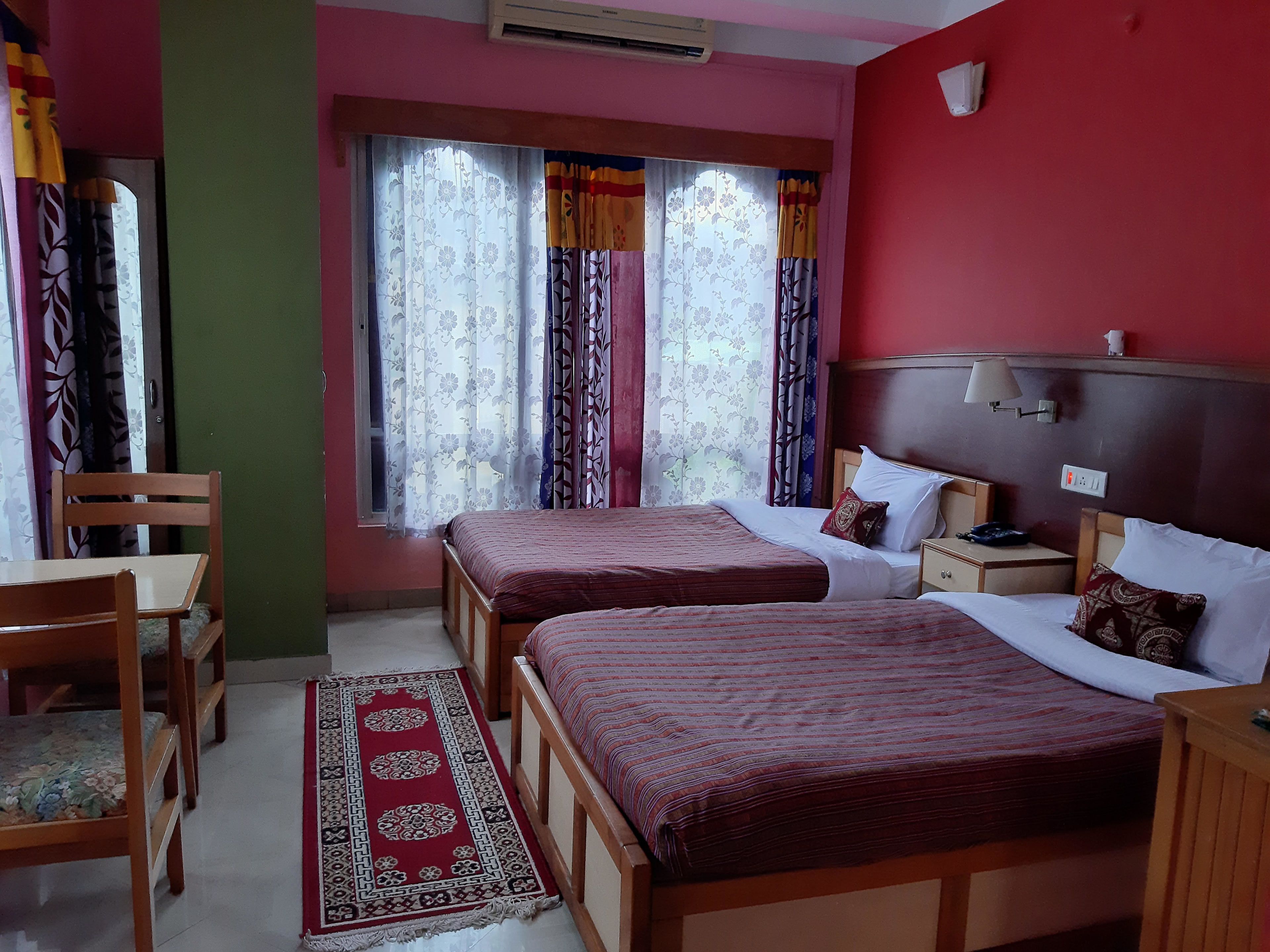 A hotel room with two beds, a desk, a chair, and a window with curtains.