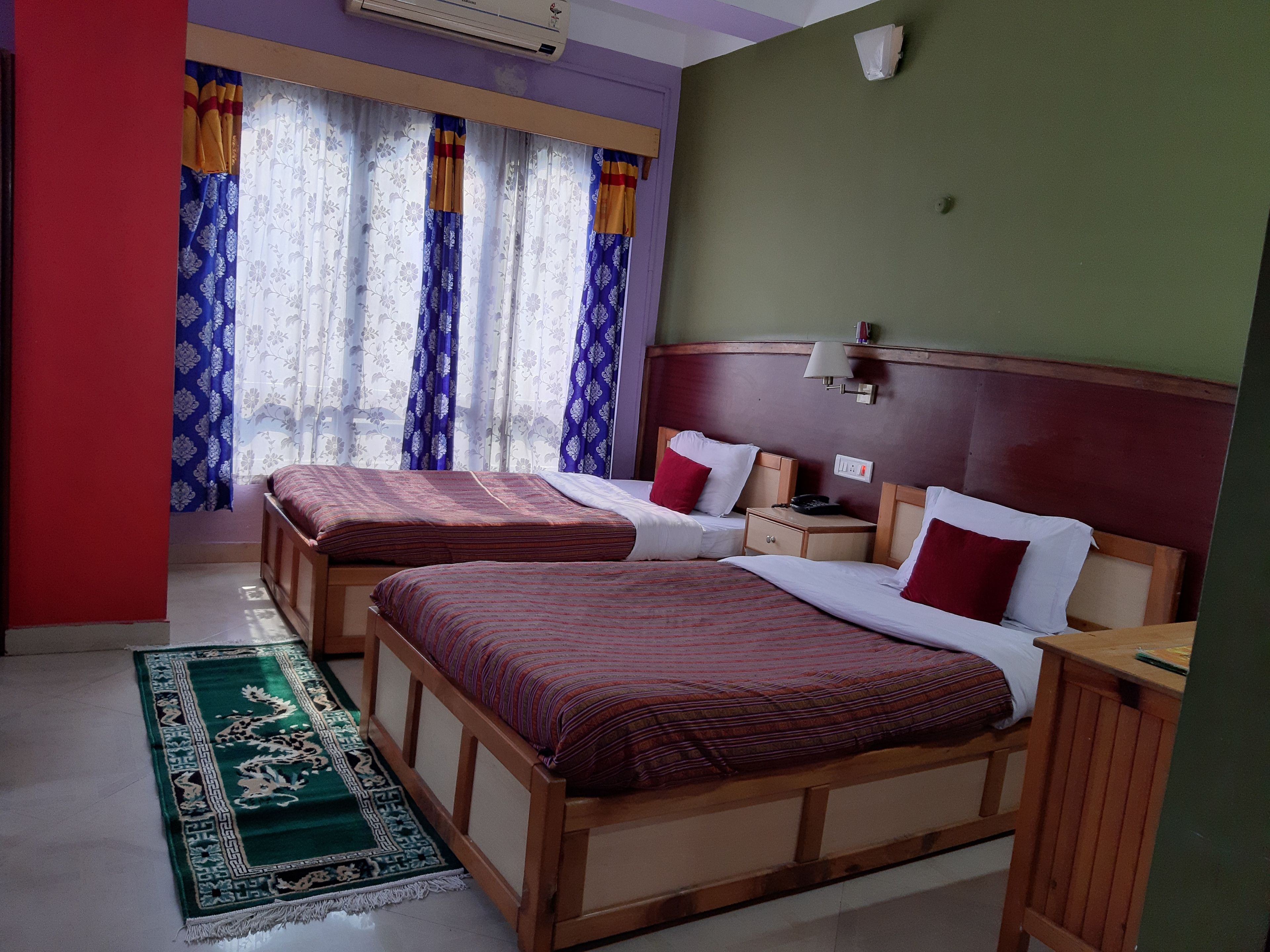 A hotel room with two wooden beds, a green carpet, and a window with floral curtains.