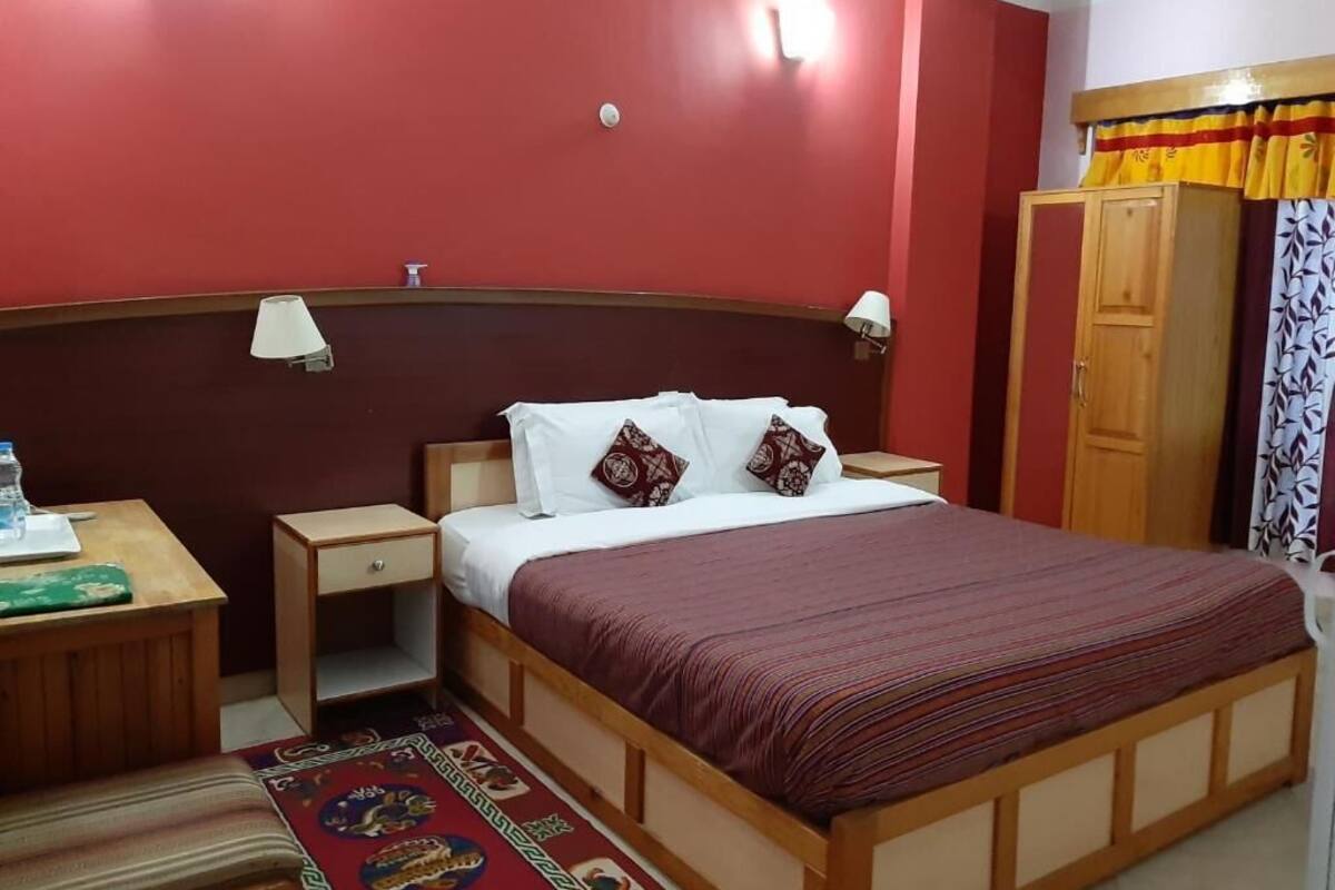 A hotel room with a wooden bed, two bedside tables, a nightstand, a red wall, and a wardrobe.
