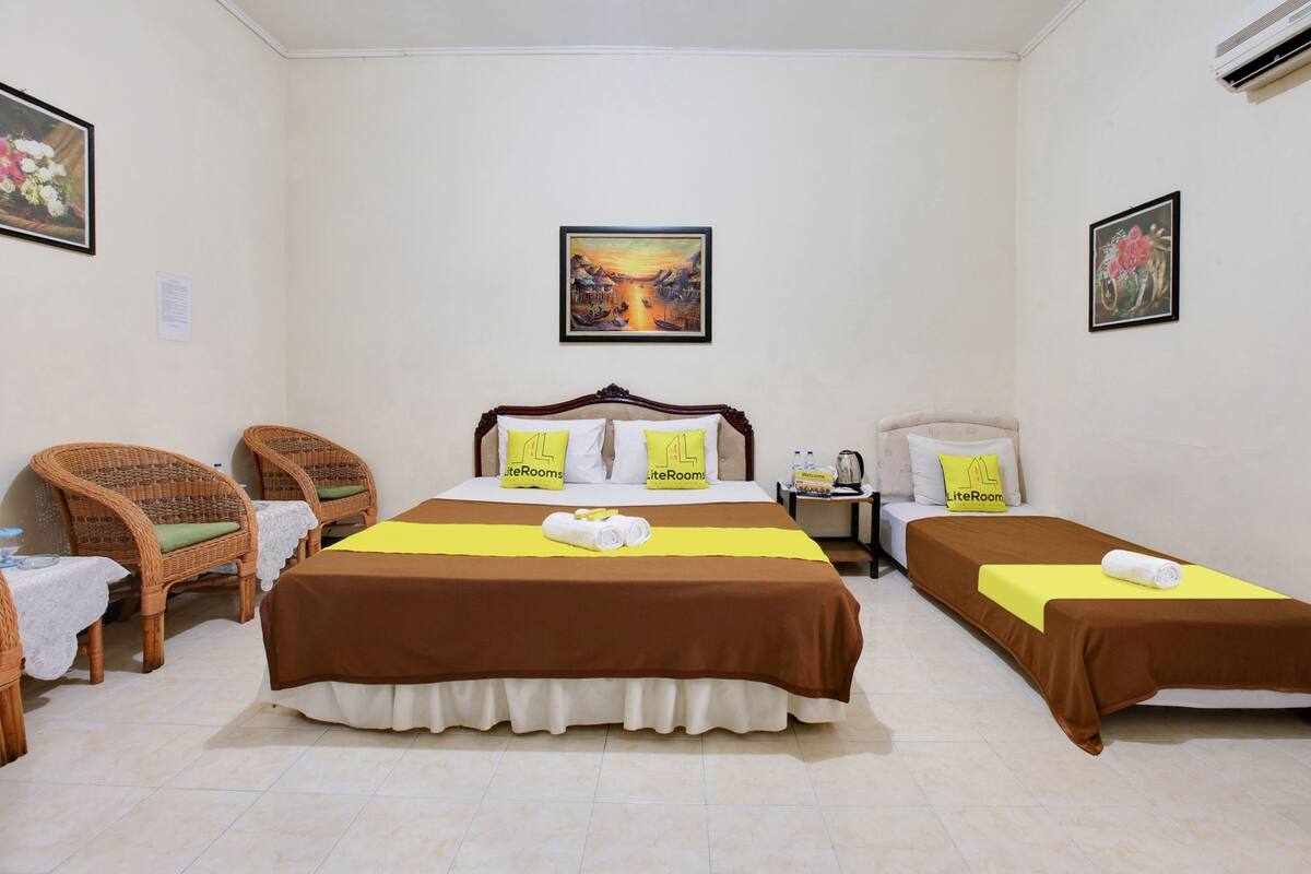 A hotel room with two beds, wicker chairs, a table with a lace tablecloth, and artwork on the walls.