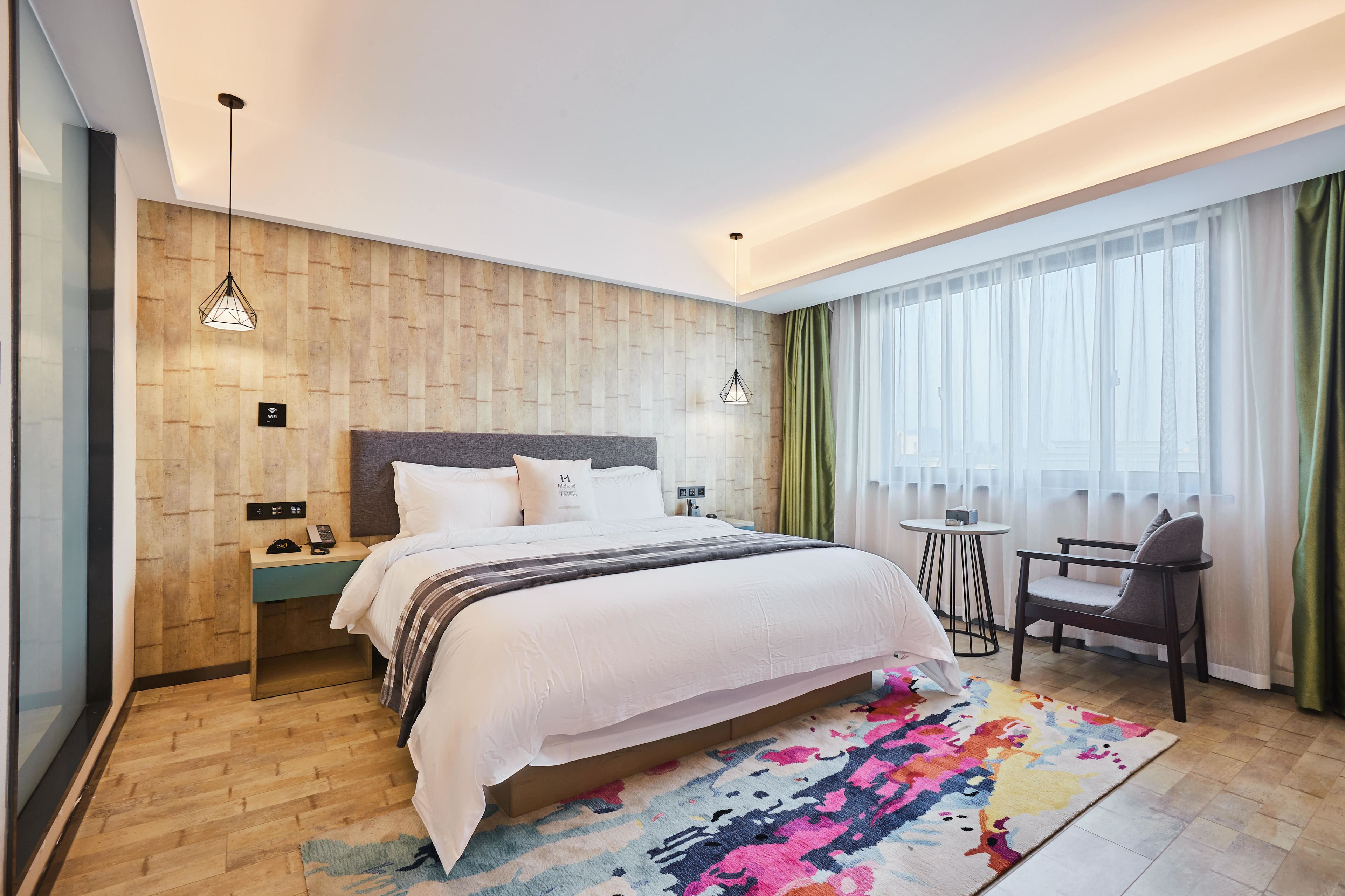 Une chambre d’hôtel moderne avec un mur en bois, un grand lit, un petit bureau, une chaise et un tapis coloré.