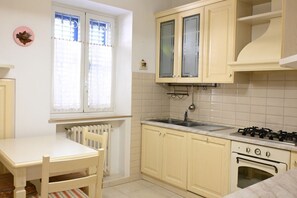 A kitchen with a white table, a window with curtains, a stove, and cabinets.