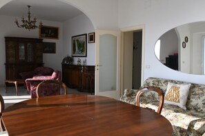 A dining area with a wooden table and chairs, a floral sofa, and a mirror reflecting part of the room.