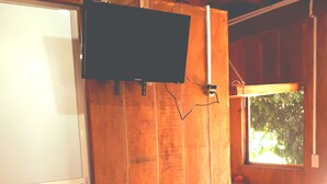 Ein Zimmer mit Holzwänden, einem Bett mit weißer Bettdecke und einem an der Wand befestigten Fernseher.